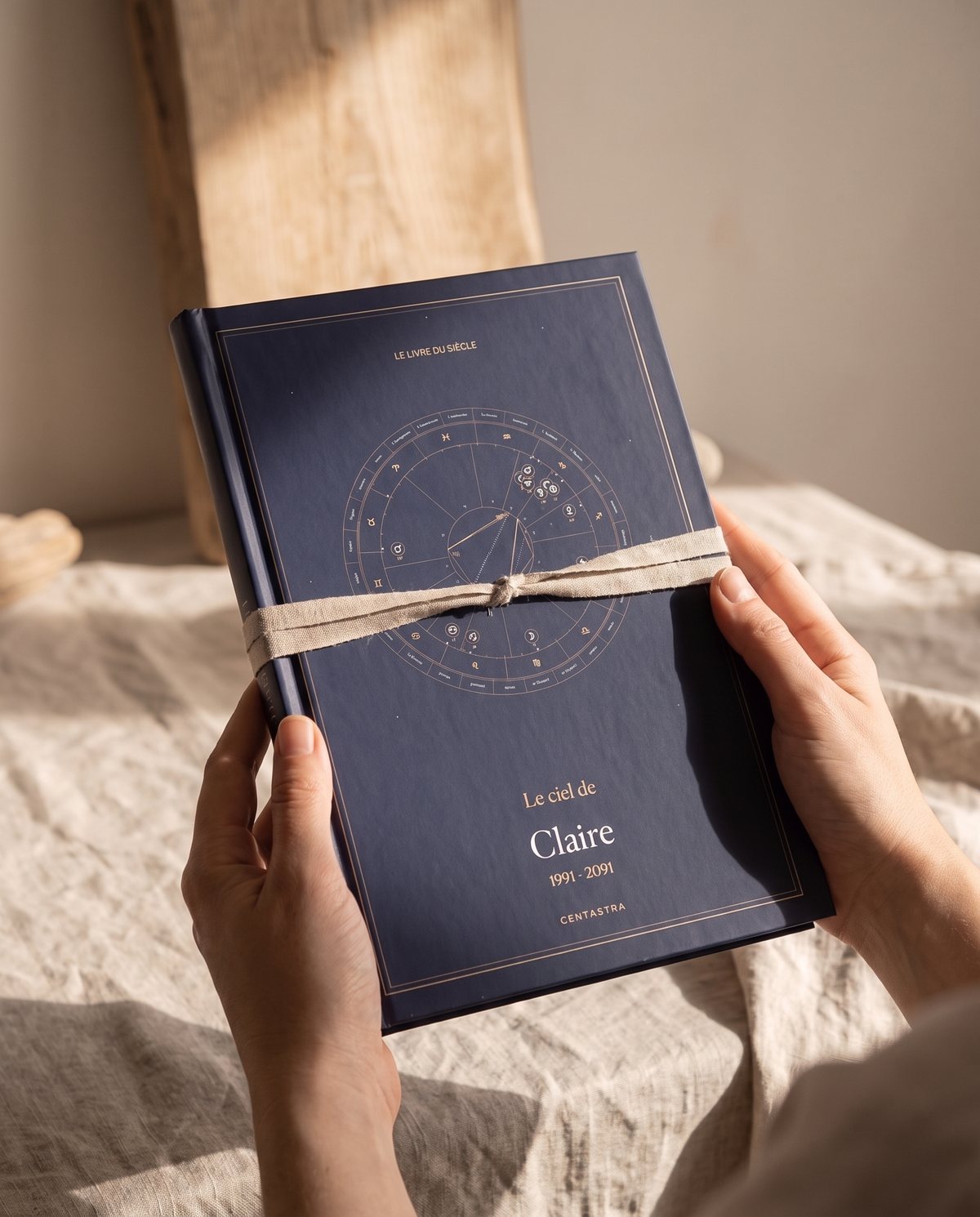 Le livre Centastra, couverture bleu nuit à la carte céleste, noué d'un ruban, posé sur du lin